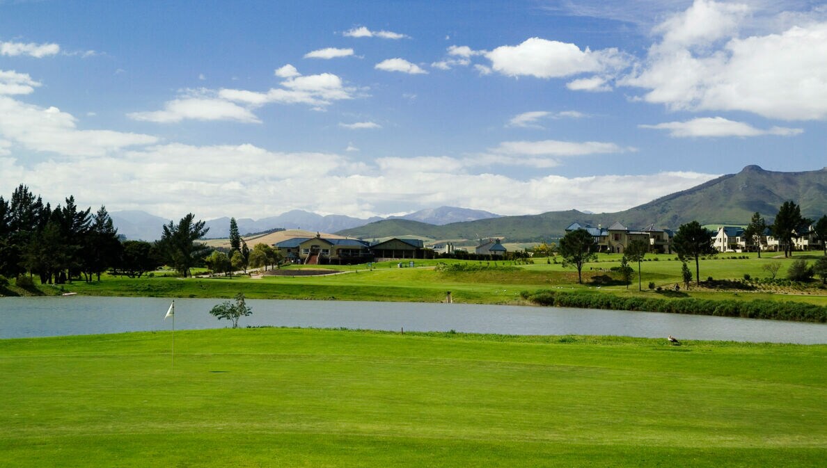Blick auf einen Golfplatz mit See und Bergen im Hintergrund