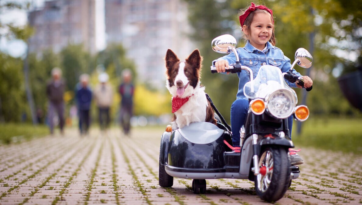 Kleines Mädchen mit Hund auf einem Kindermotorrad
