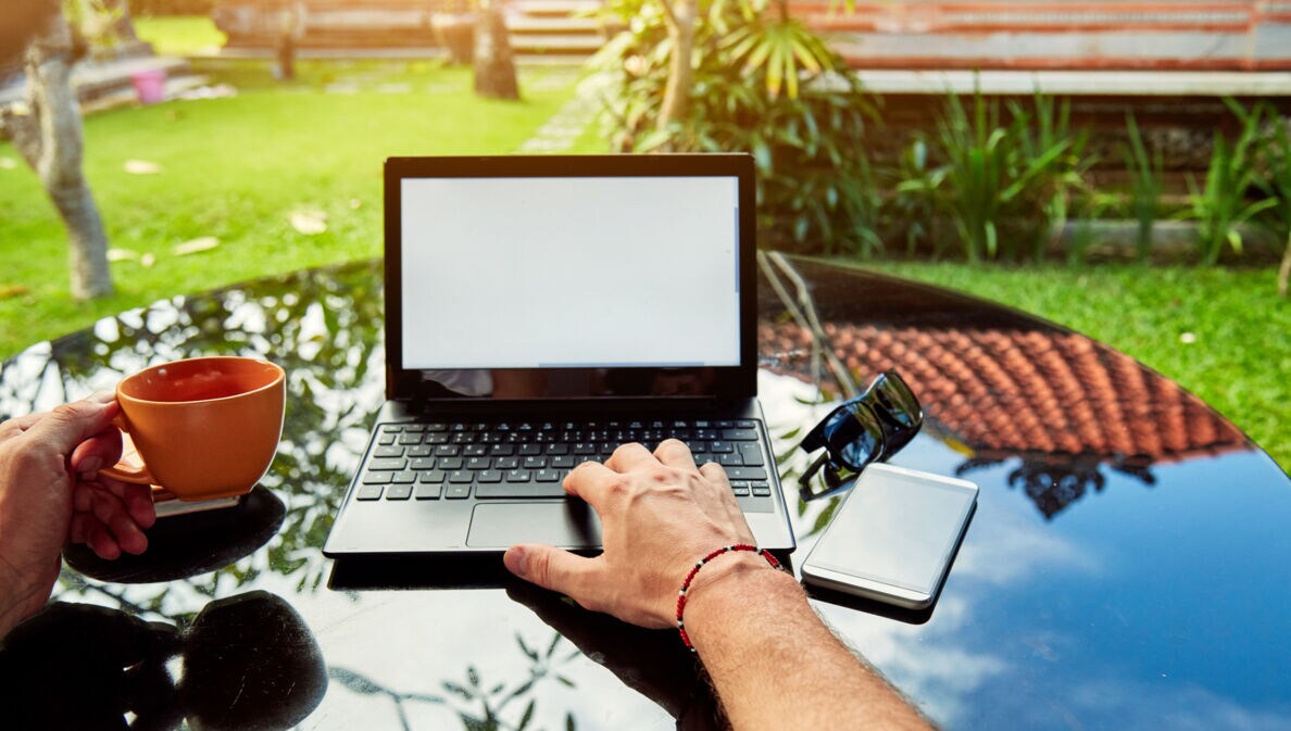 Blick auf einen Laptop, der auf einem Tisch in einem tropischen Garten steht.