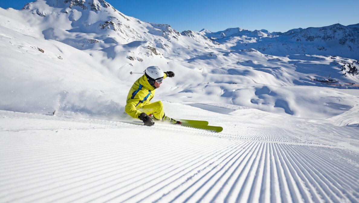 Ein Skifahrer im gelben Skianzug in Kurvenlage auf einer Piste