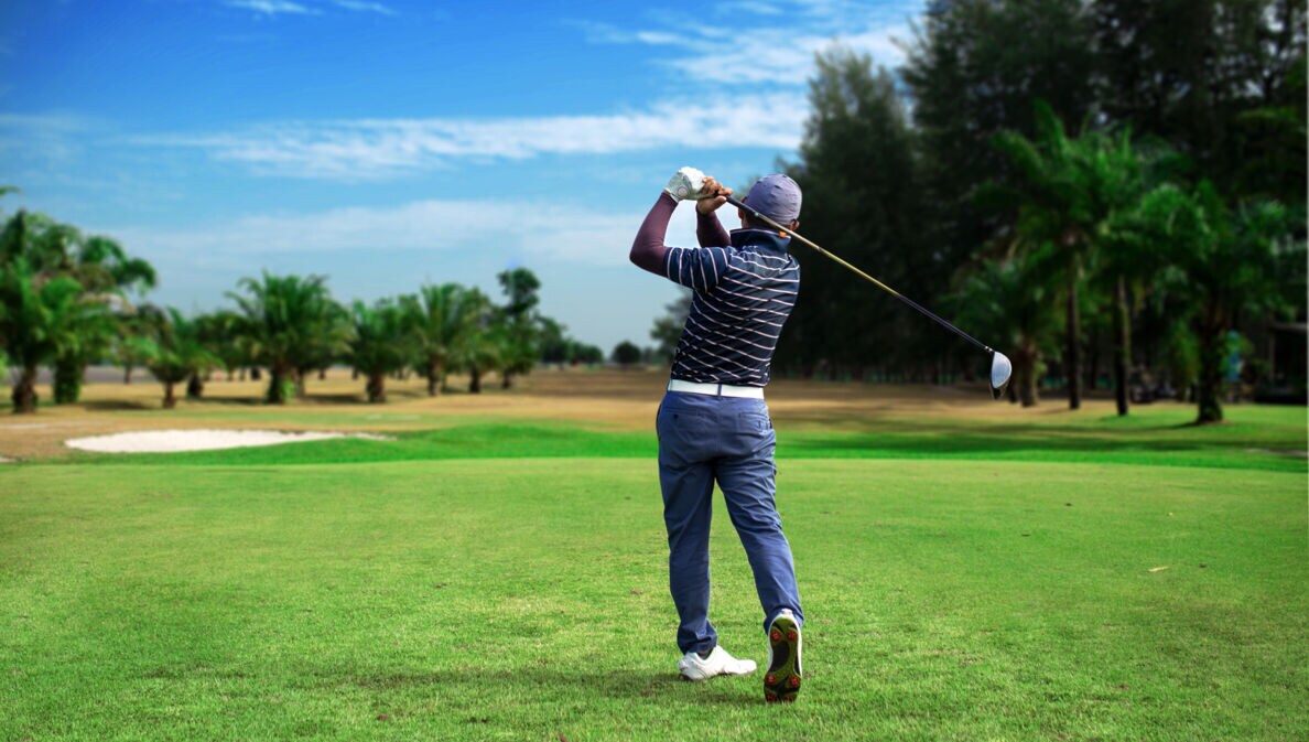 Ein Golfspieler von hinten auf einem Golfplatz, im Hintergrund Palmen