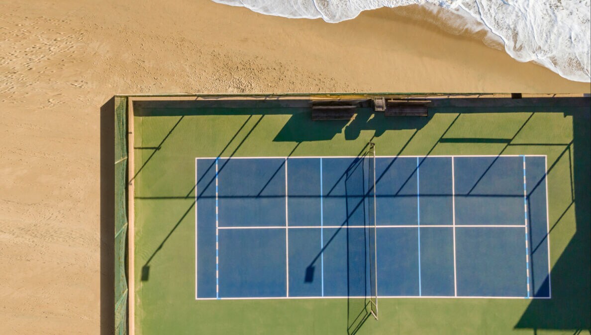 Drohnenansicht des Tennisplatzes am Sand und Meer.
