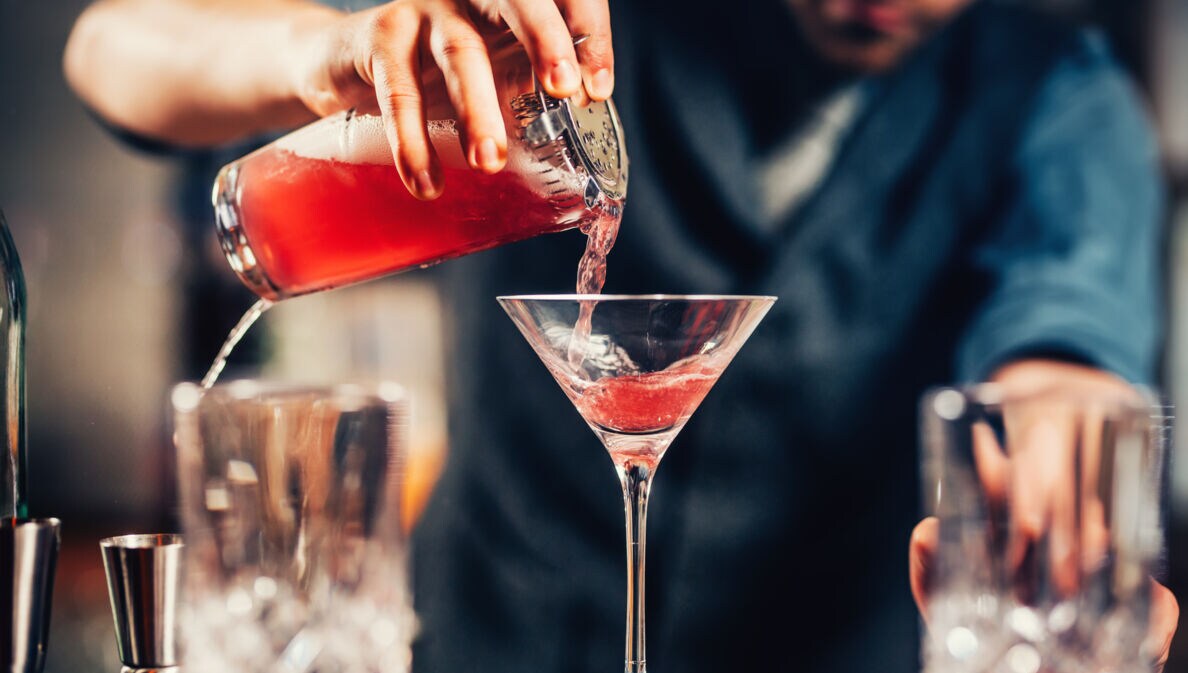 Nahaufnahme eines Cocktailglases, das von einem Barkeeper mit einer roten Flüssigkeit gefüllt wird