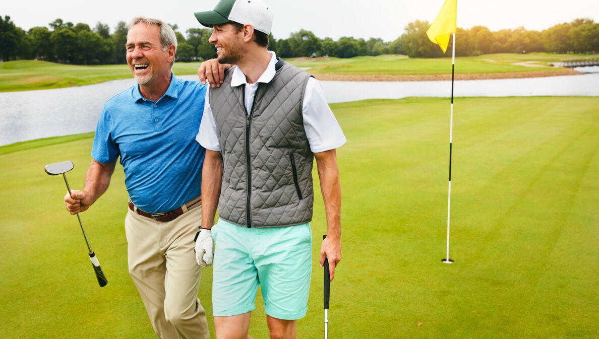 Zwei Golfspieler laufen über einen Golfplatz und lachen