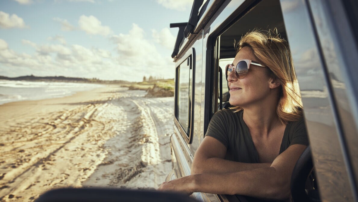 Eine lächelnde Frau mit Sonnenbrille in einem Auto am Strand