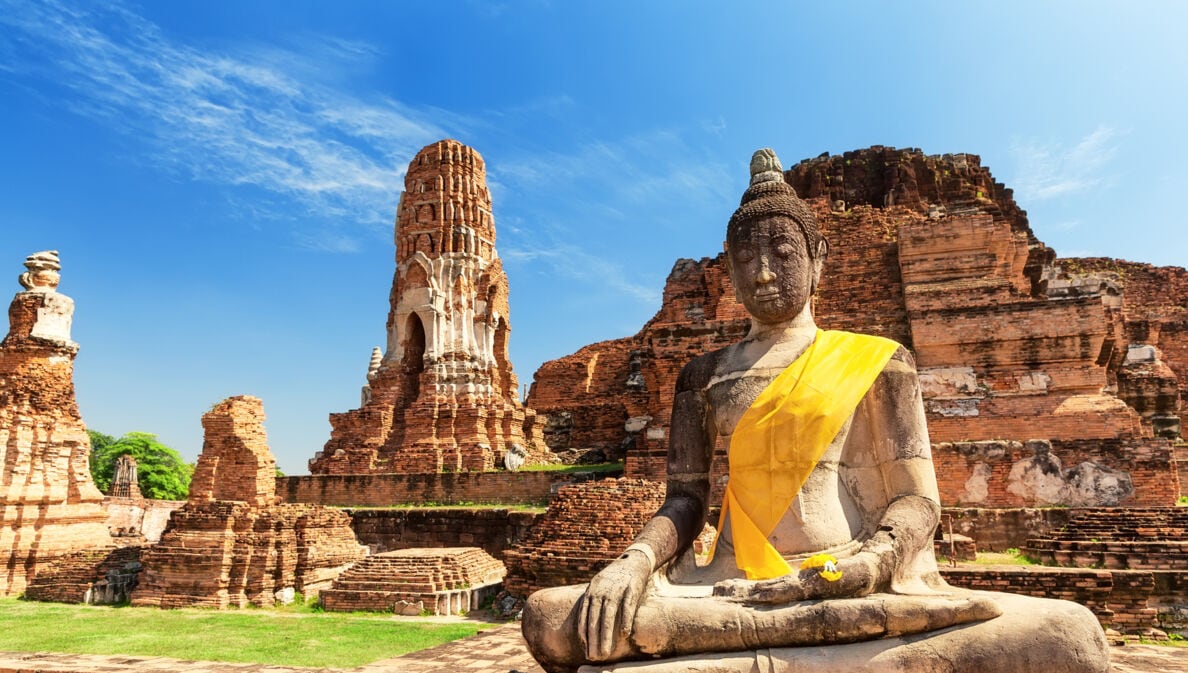 Eine Buddhastatue vor Ruinen eines Tempels