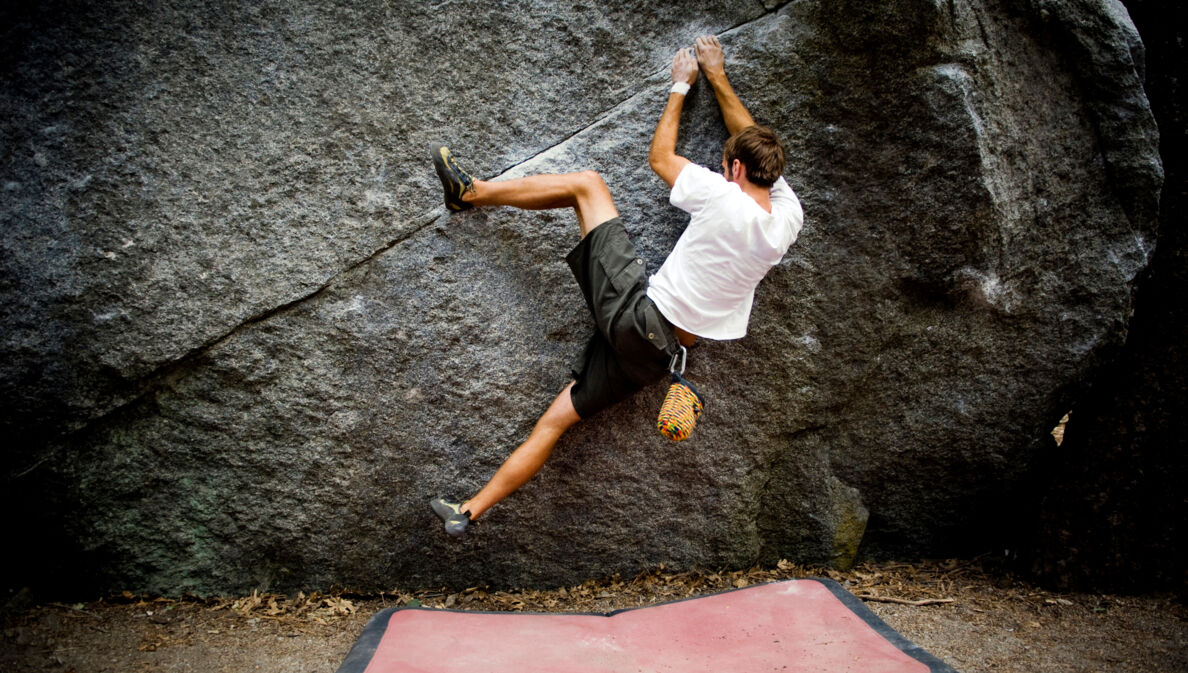 Eine Person klettert ohne Seil knapp über dem Boden an einer Felswand entlang, unter ihr liegt eine Matte