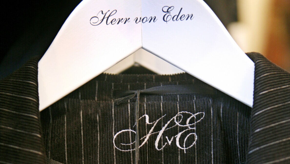 Detailaufnahme eines Nadelstreifenanzugs auf einem weißen Kleiderbügel mit einer geschnörkelten Aufschrift