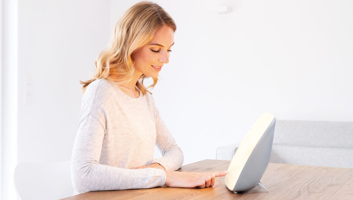 Eine junge Frau sitzt an einem Tisch vor einer Tageslichtlampe