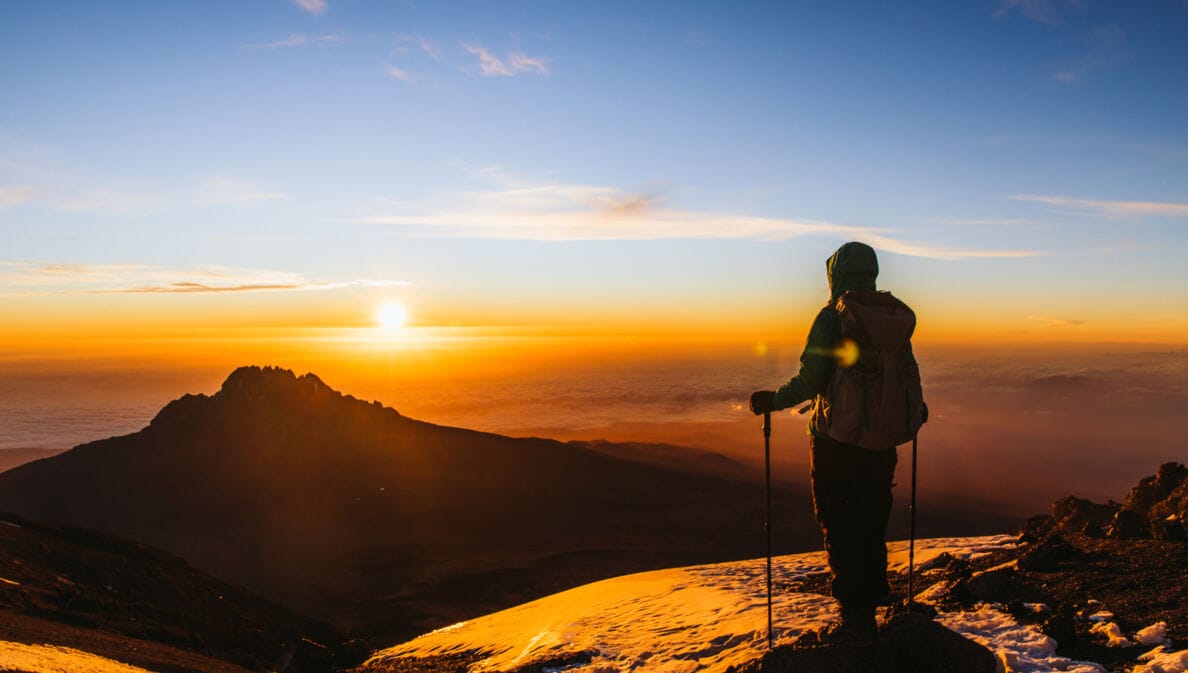 Eine Wanderin blickt vom Gipfel des Kilimandscharo in den Sonnenaufgang
