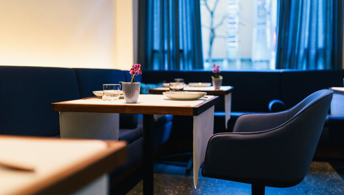 Drei eingedeckte, viereckige Holztische im Restaurant Tim Raue und blaue, gepolsterte Stühle