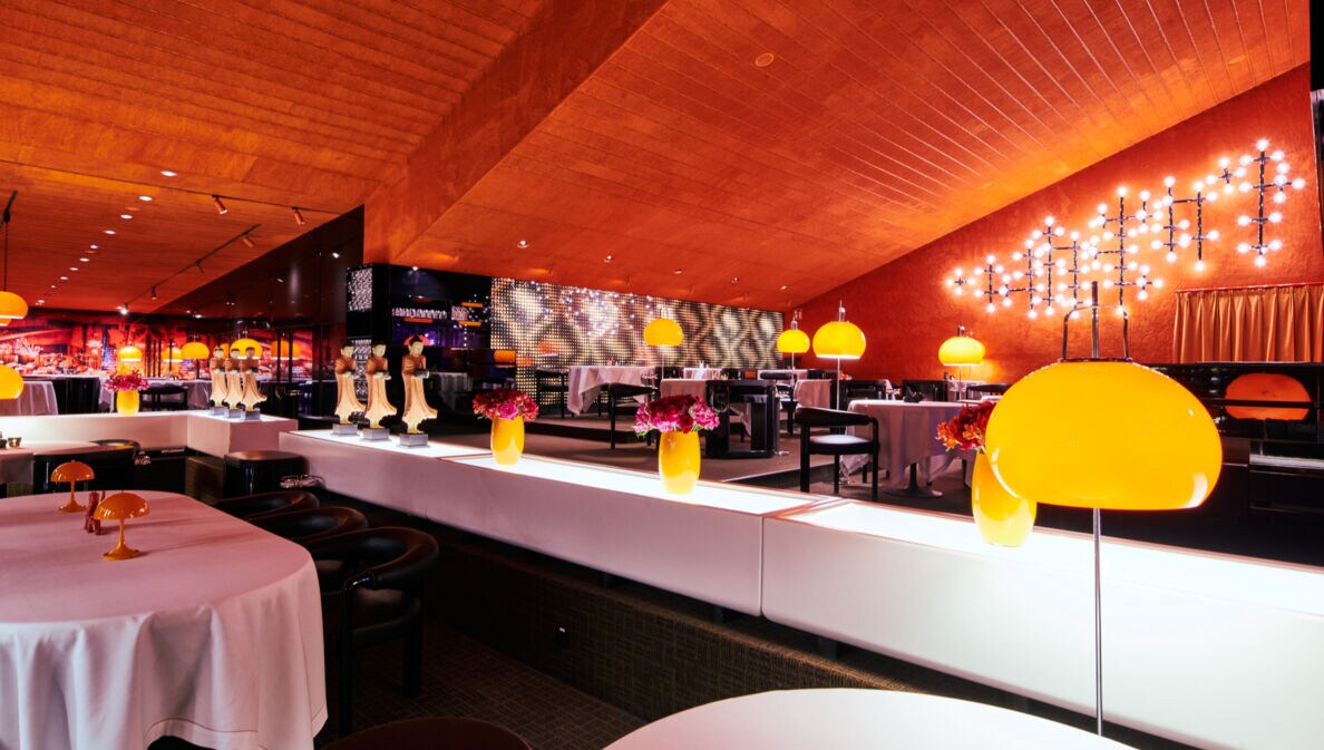 Ein elegantes Restaurant mit weißem Trennelement, gedeckten Tischen, einer getönten Decke und orangenen Designerlampen