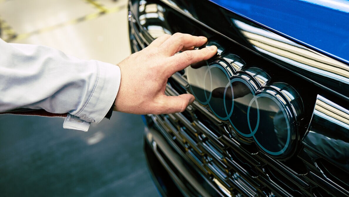 Eine Hand berührt die Audi-Ringe an einem Pkw.