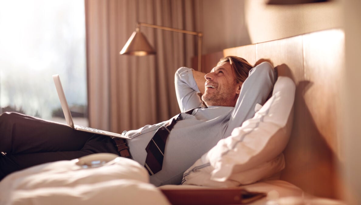 Ein Geschäftsmann liegt entspannt mit einem Laptop in einem Hotelbett