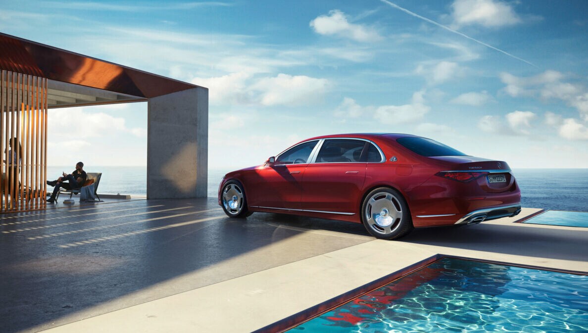 Ein roter Mercedes-Maybach von der Seite am Pool eines modernen Hauses, im Hintergrund Meer und Personen im Haus