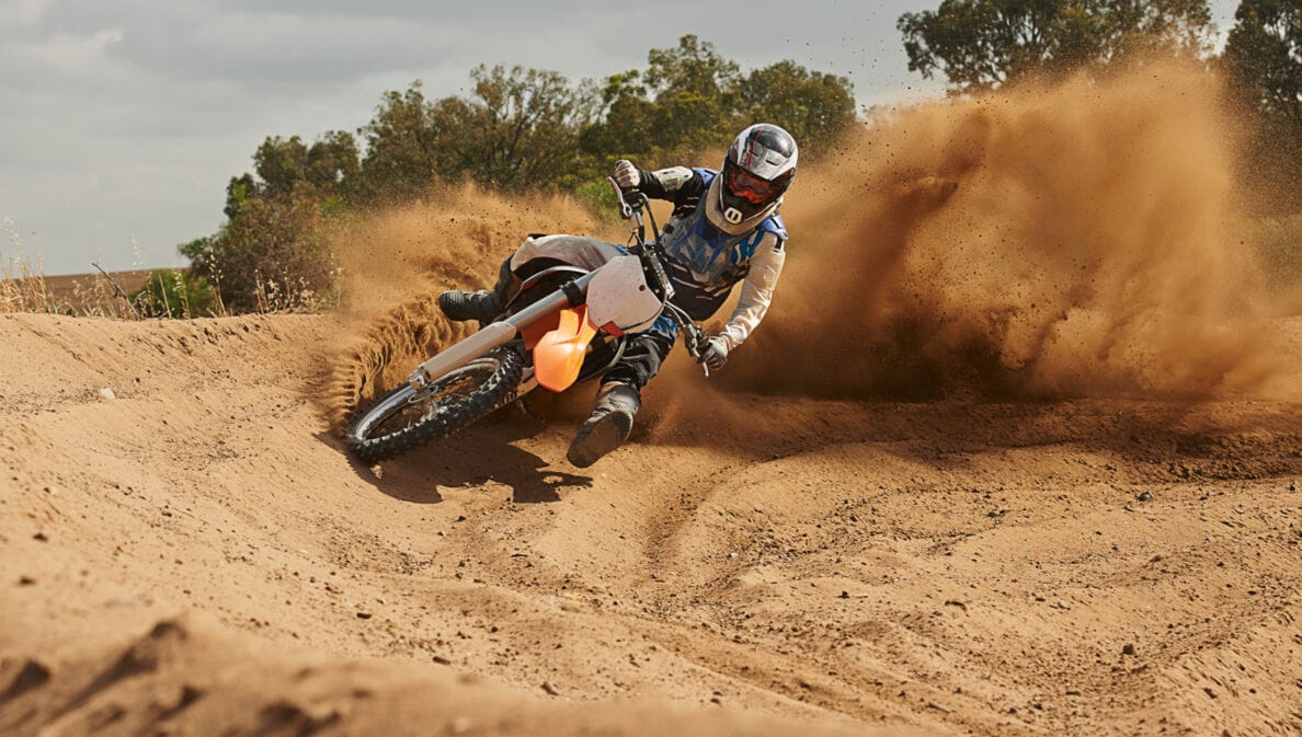 Eine Person fährt auf einem Motocrossbike um die Kurve und wirbelt Sand auf