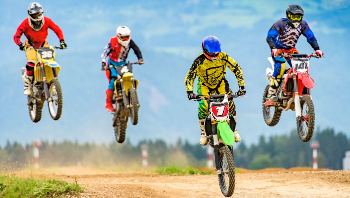 Vier Fahrer springen mit ihren Motocrossmotorrädern über eine Rennpiste