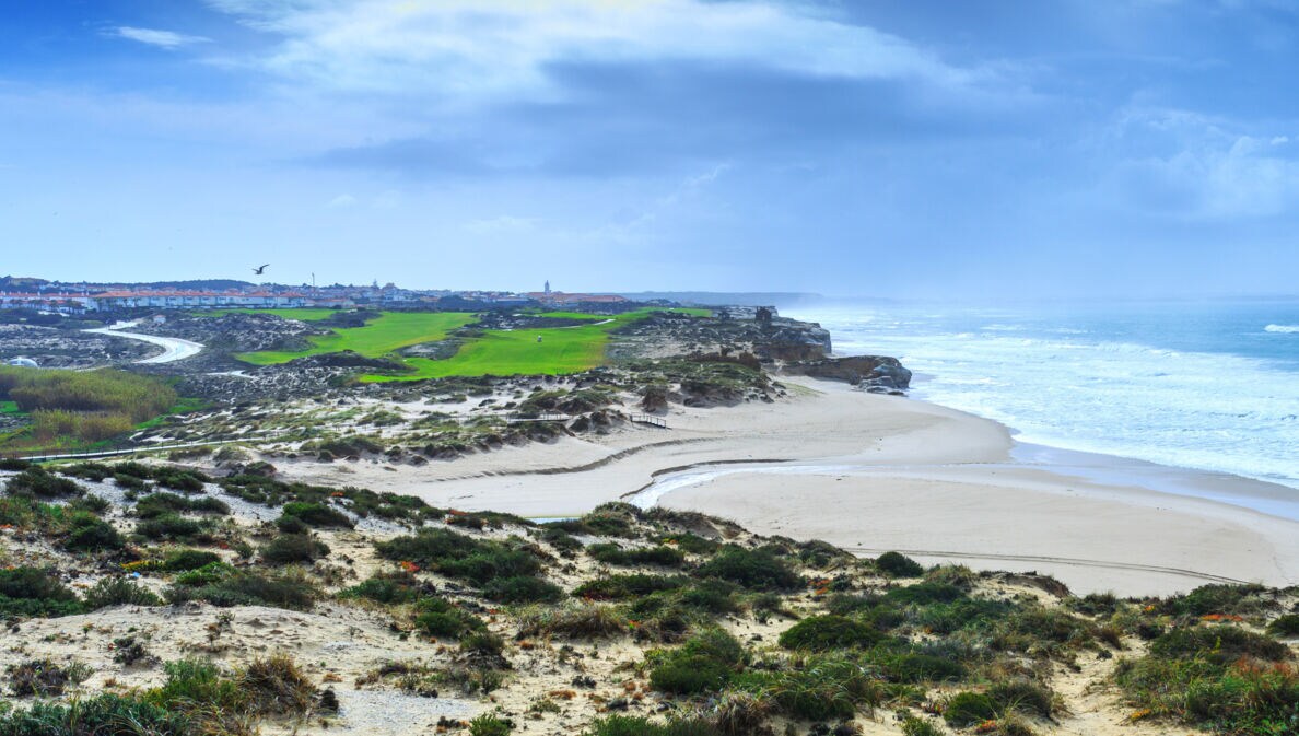 Ein hügeliger Golfplatz neben einem Sandstrand an einem wilden Küstenabschnitt