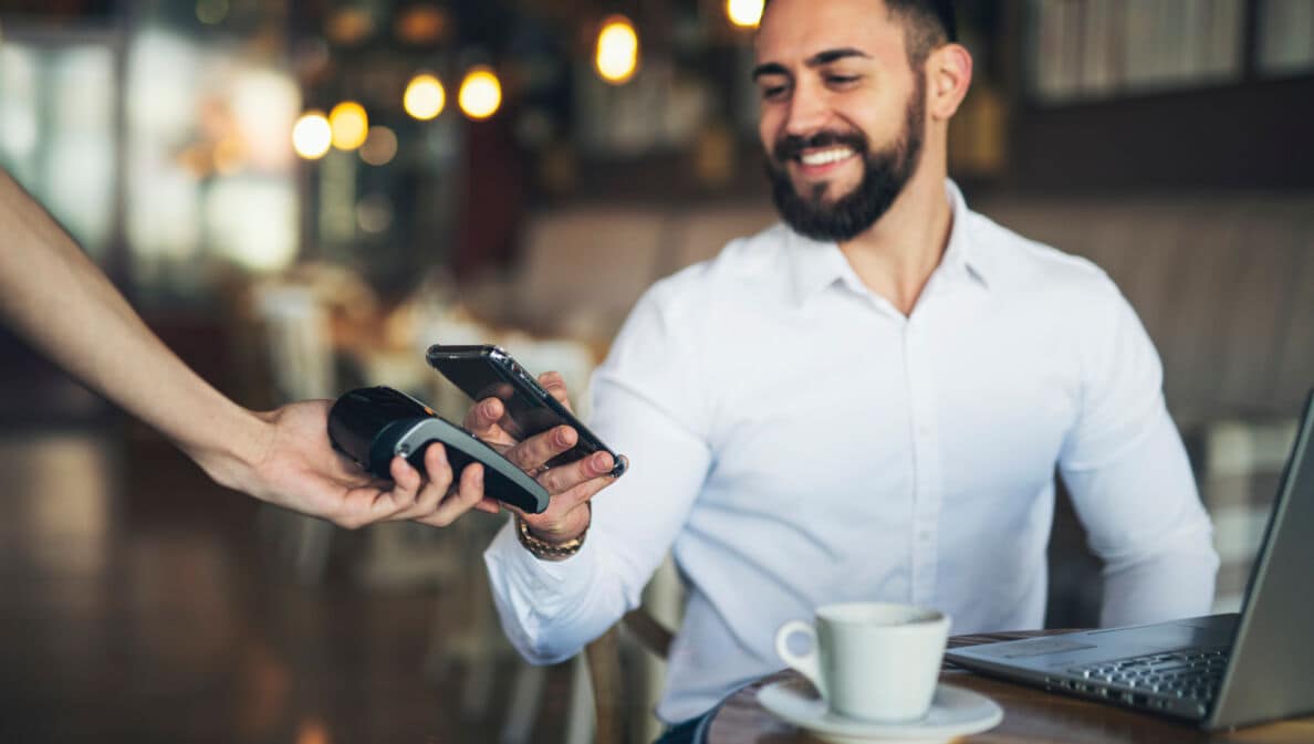 Ein junger Mann bezahlt kontaktlos mit seinem Smartphone in einem Café