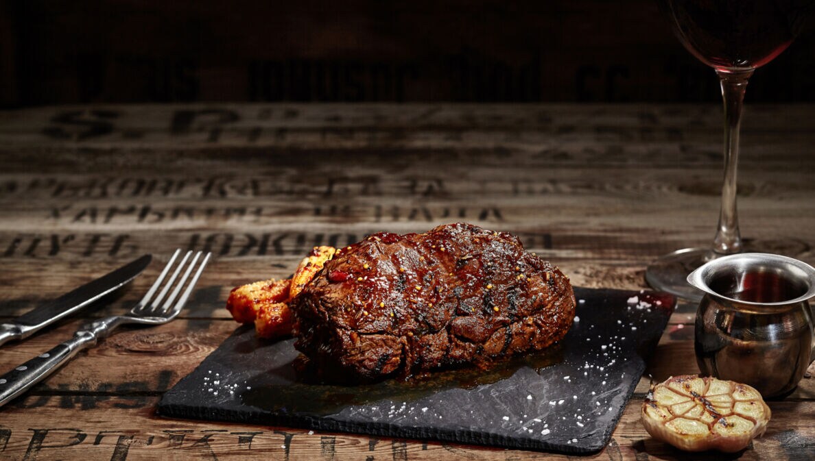 Ein gebratenes Steak liegt auf einer Granitplatte auf einem Holztisch