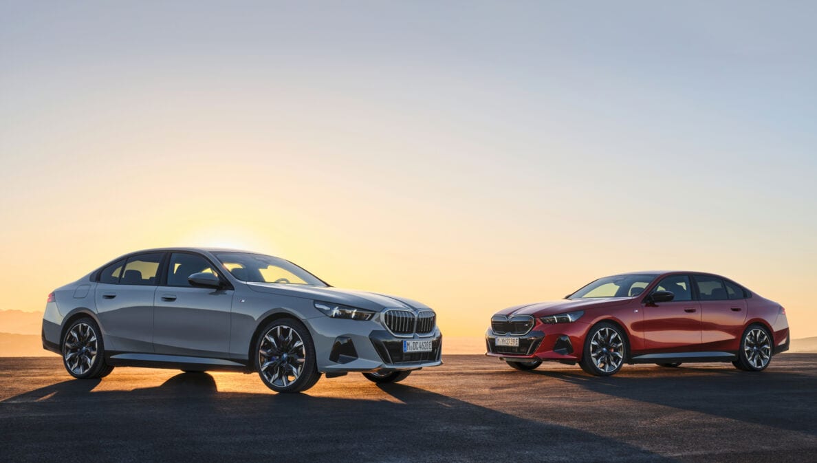Zwei BMW i5, einmal in Silber, einmal in Rot, die von hinten von der Sonne angestrahlt werden.