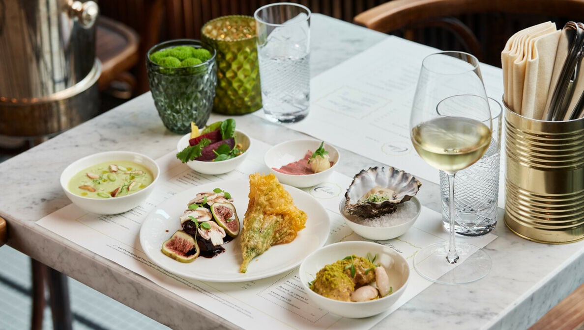 Mehrere Teller mit feinen Speisen und ein Glas Weißwein stehen auf einem Marmortisch