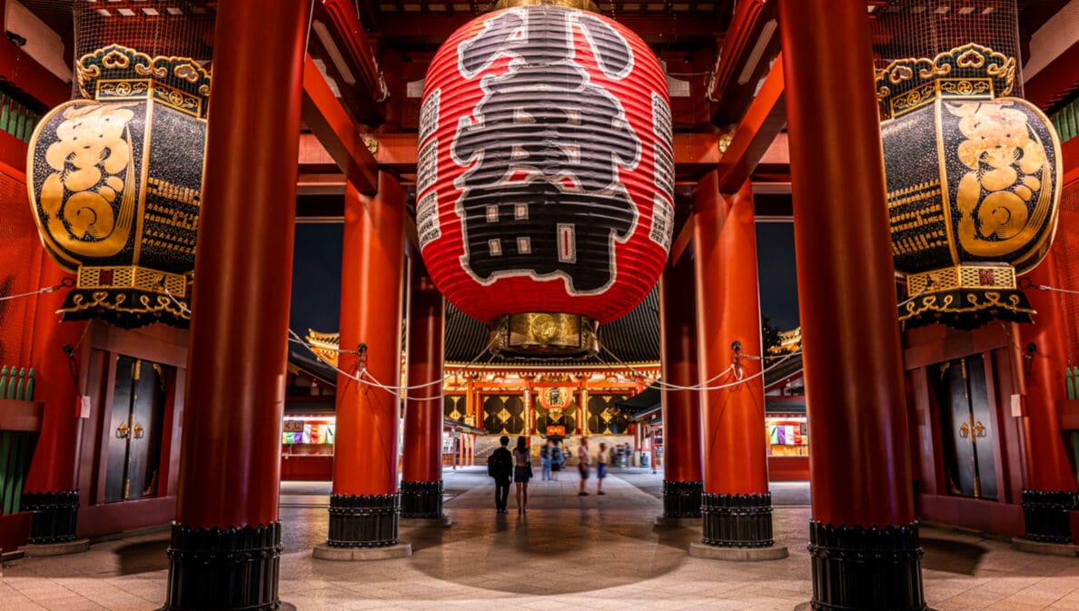 Rote Säulen und überdimensionale Laternen mit japanischen Schriftzügen in einem Tempel