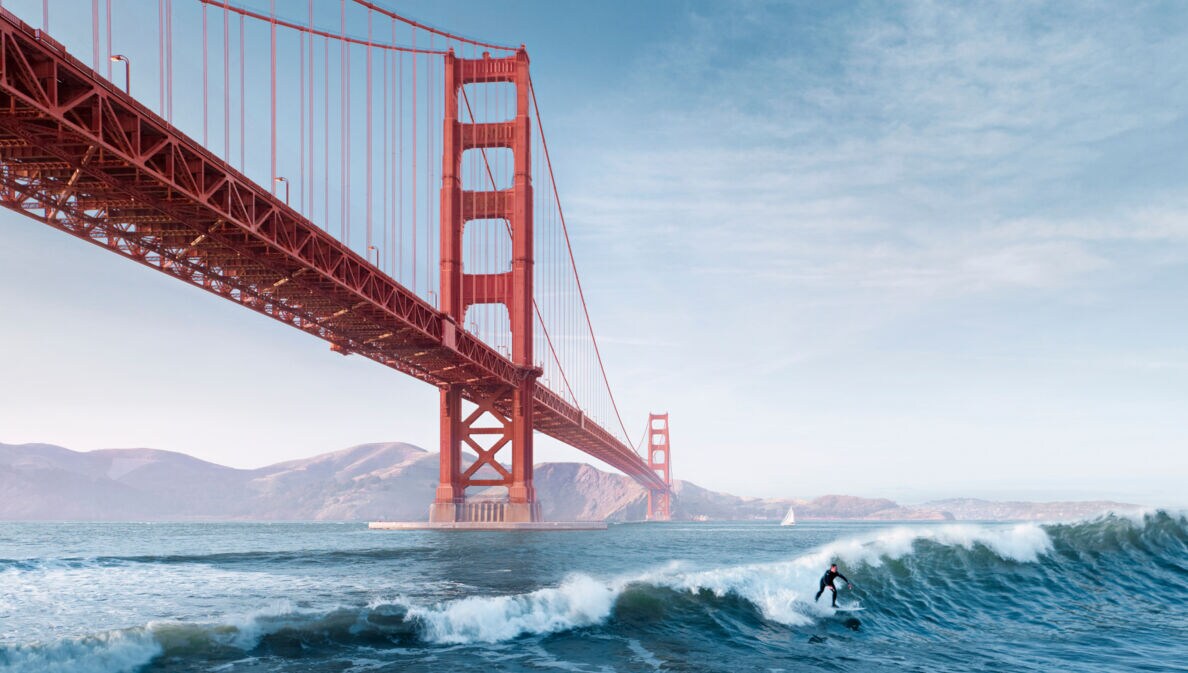 Ein Surfer auf einer Welle unter der roten Golden Gate Bridge