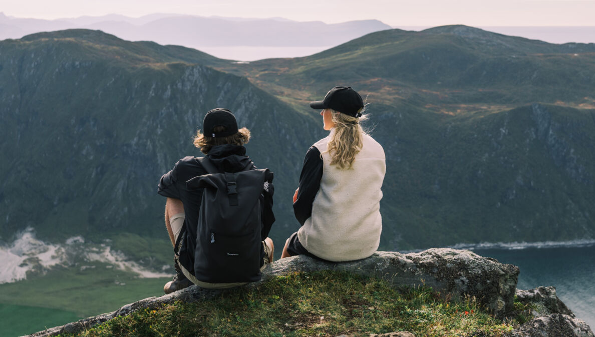 Eine Frau und ein Mann sitzen auf einem Bergvorsprung und schauen in die Ferne