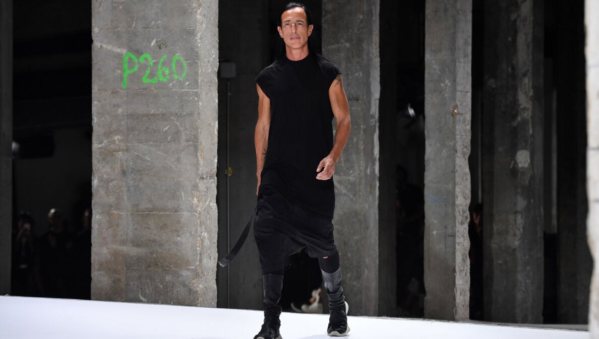 Designer Rick Owens in einem schwarzen, lässigen Kleid läuft in einer Industriehalle über einen Lauftsteg