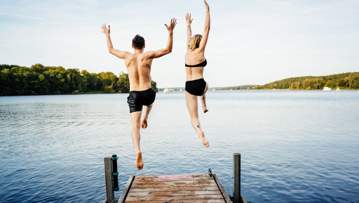 Rückansicht eines Paares in Badekleidung, das von einem Steg in einen See springt