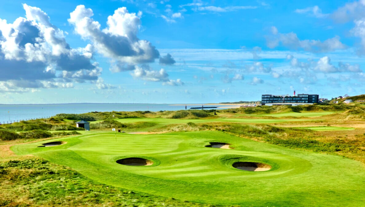 Grüner Golfplatz mit runden Bunkern mit Hotel und Meer im Hintergrund