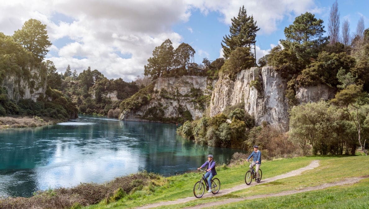 Ein Paar auf Fahrrädern fährt auf einem Radweg entlang eines Sees, umgeben von bewaldeten Felsen