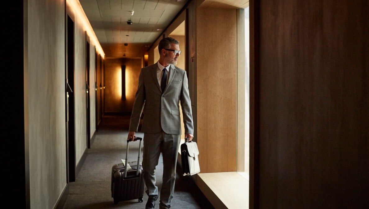 Ein Mann in Anzug zieht einen Businesstrolley über einen Hotelflur