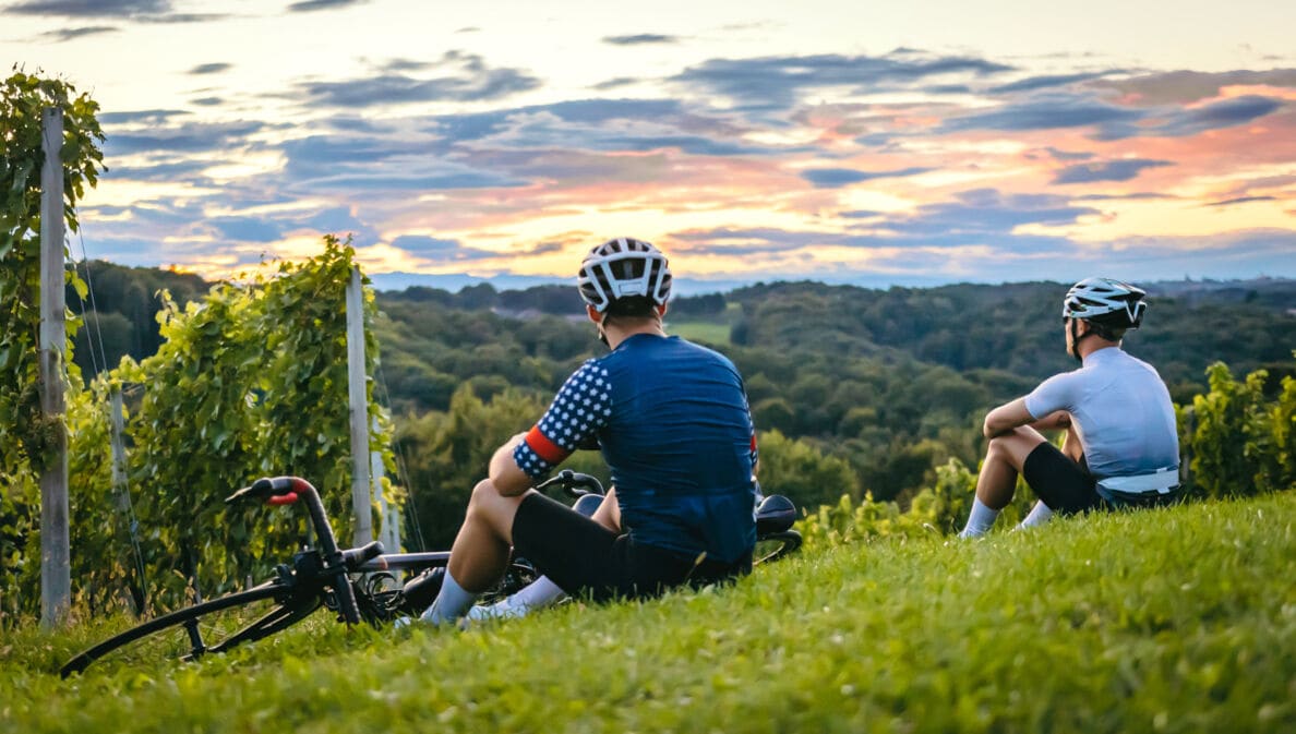 Rückenansicht zweier Personen in Fahrradkleidung, die auf einem Weinberg sitzen