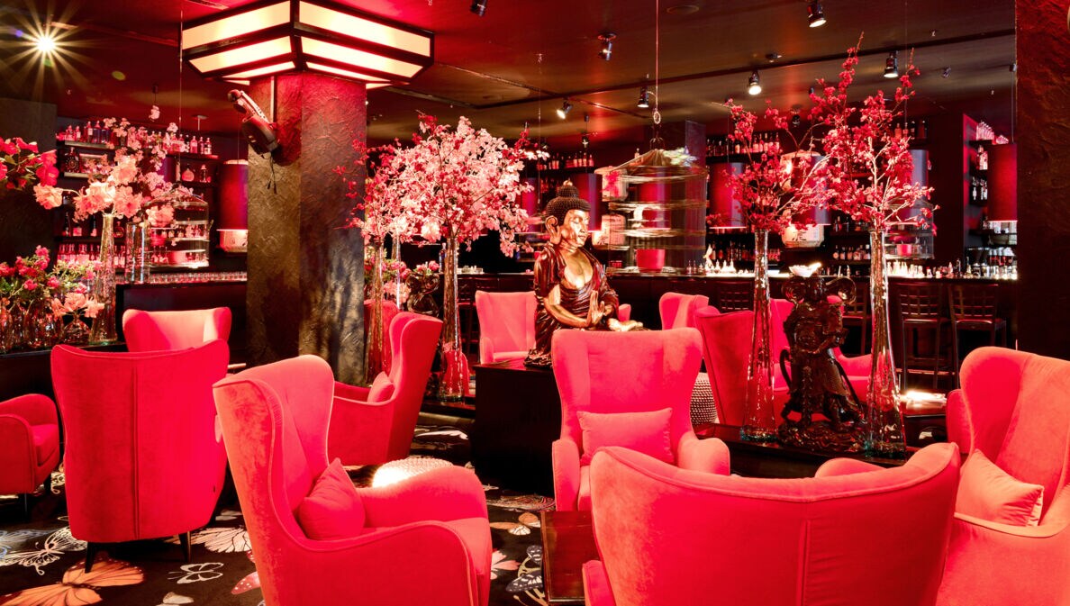 Beleuchtete, elegante Bar mit asiatischem Dekor und pinken Samtseseln.