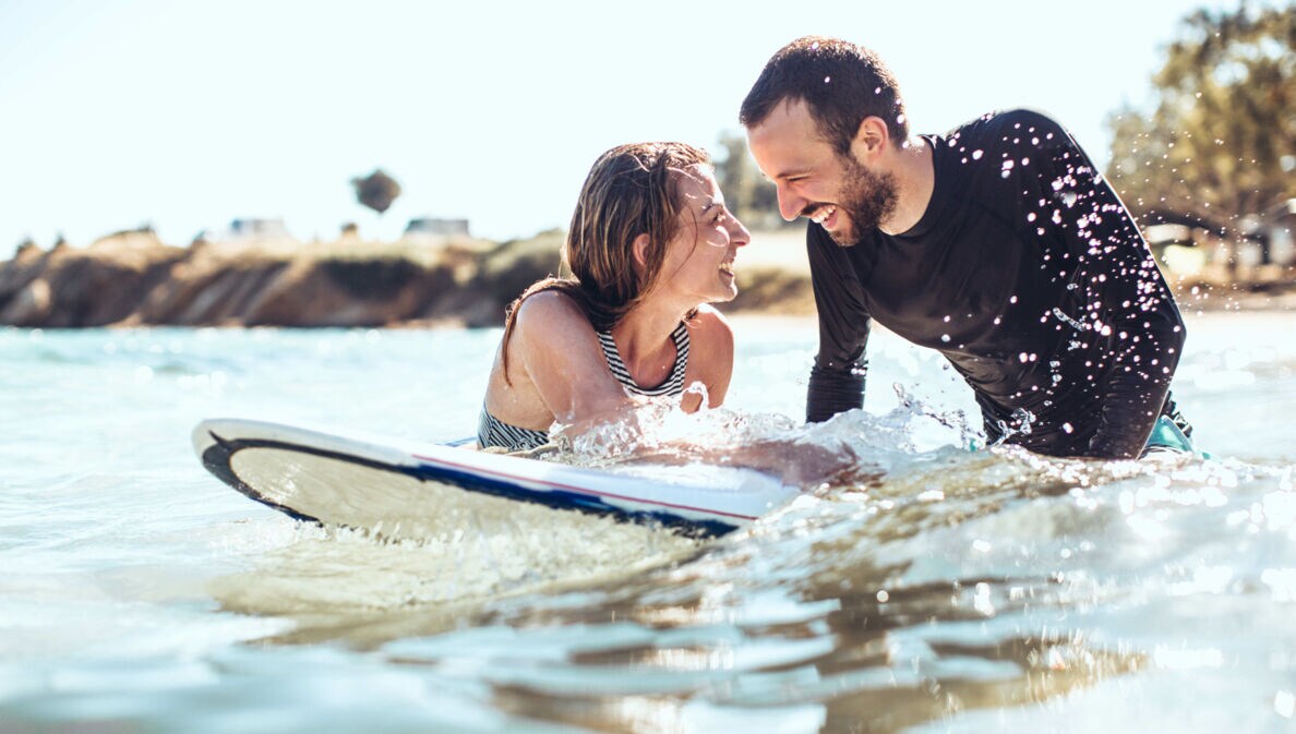 Ein lachendes Paar im Meer auf einem Surfboardon-Surfer