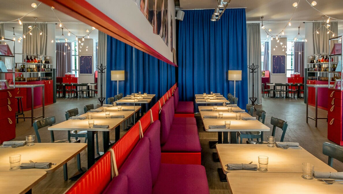 Modernes Restaurant mit hellen Holztischen und roten Sitzbänken an einer Spiegelwand.
