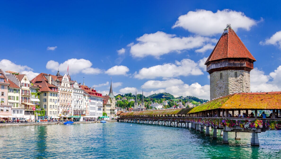 Altstadtpanorama von Luzern am Wasser mit einer hölzernen Brücke vor einem Wasserturm.