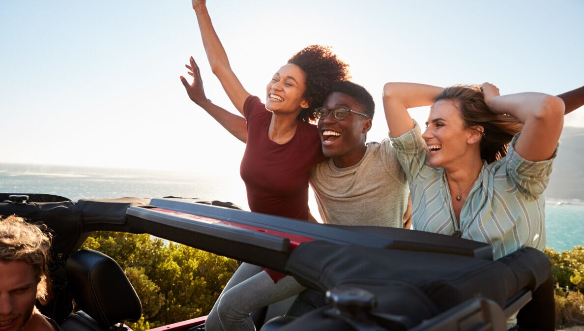 Aufgeregte Freunde, die mit erhobenen Armen auf dem Rücksitz eines offenen Autos reisen