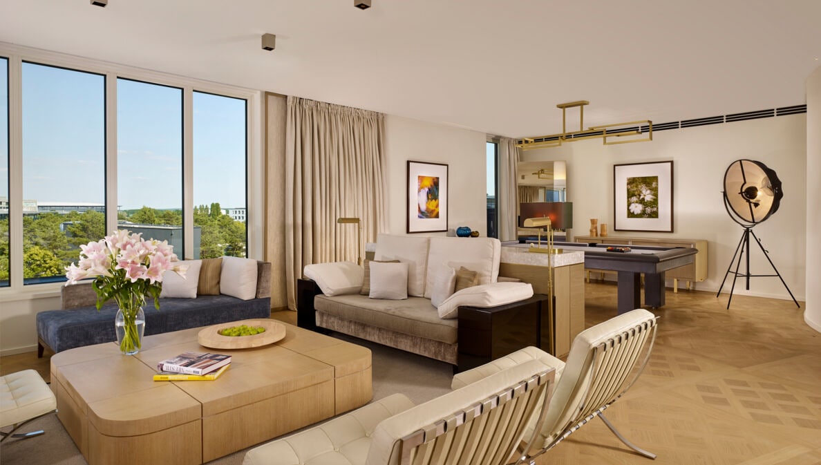 Eine modern und mit hellem Mobiliar eingerichtete Hotel-Suite mit großer Fensterfront.