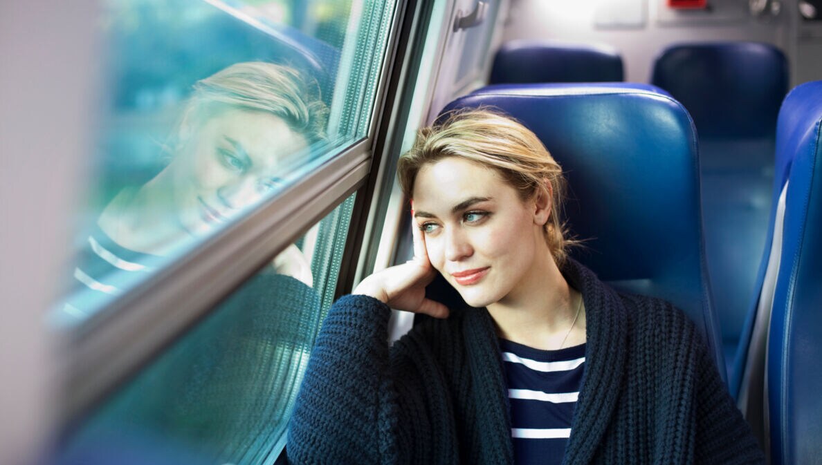 Eine Frau sitzt im Zug und schaut aus dem Fenster.