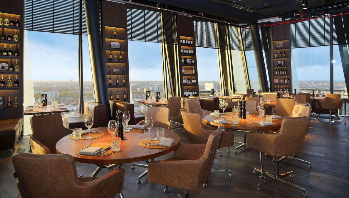 Das clouds Restaurant in Hamburg mit dunklem Ambiente, Ledersesseln, warmer Beleuchtung und runden Holztischen.