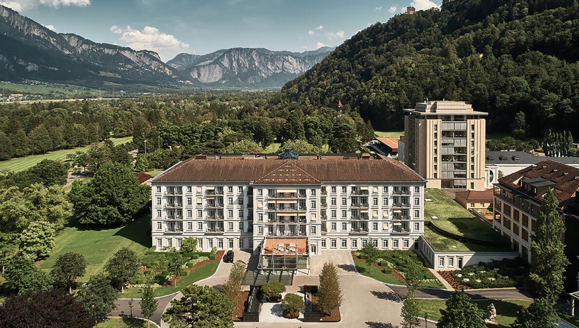 Luftansicht des Grand Resort Bad Ragaz in der Schweiz umgeben von grüner und waldiger Landschaft. Im Hintergrund Berge.