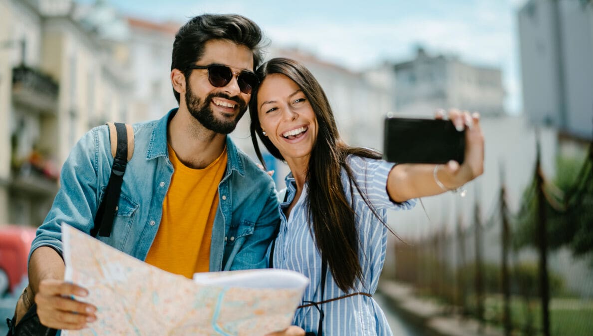 Ein fröhliches Paar mit Straßenplan beim Selfie fotografieren in urbaner Umgebung.