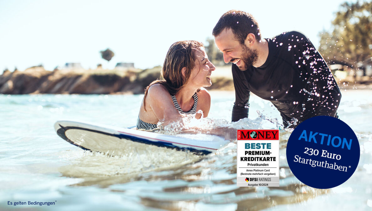 Ein lachendes Paar mit Surfboard im Meer.