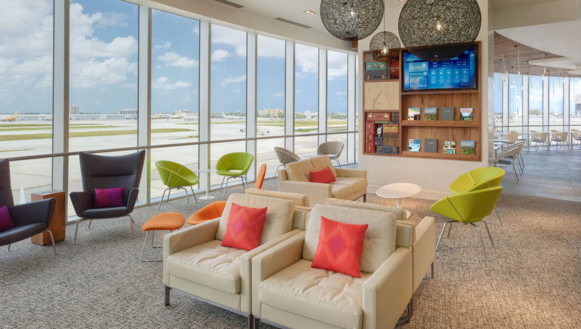 Sitzgelegenheiten in einer modernen, hellen Flughafenlounge mit Blick aufs Rollfeld durch Panoramafenster.