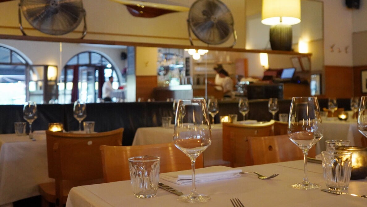 Speiseraum einer Brasserie mit eingedeckten Tischen bei gedimmtem Licht.