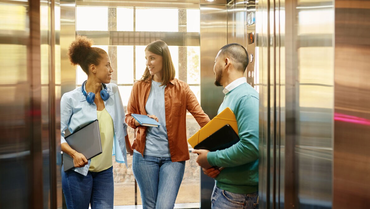 Drei Person stehen in einem Aufzug und unterhalten sich.