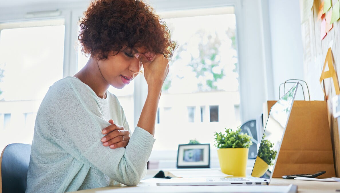 Eine Frau am Schreibtisch fasst sich an die Stirn.